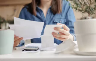 Person reviewing bills and receipts with a calculator at a casual home desk.