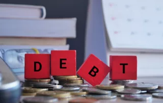 Red blocks spelling 'DEBT' atop stacked coins, surrounded by books and a calendar—symbolizing financial burden and deadlines in Chapter 13 bankruptcy completion.